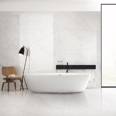 A modern bathroom with a white bathtub and a chair, featuring the Carrara marble tile with bright white background and delicate gray veining.