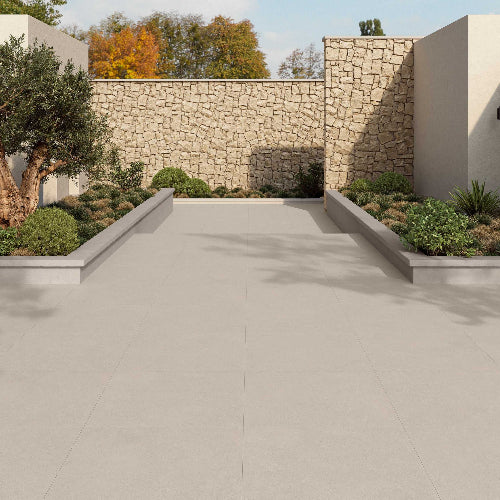 Paved pathway flanked by stone walls and garden beds with trees and shrubs.