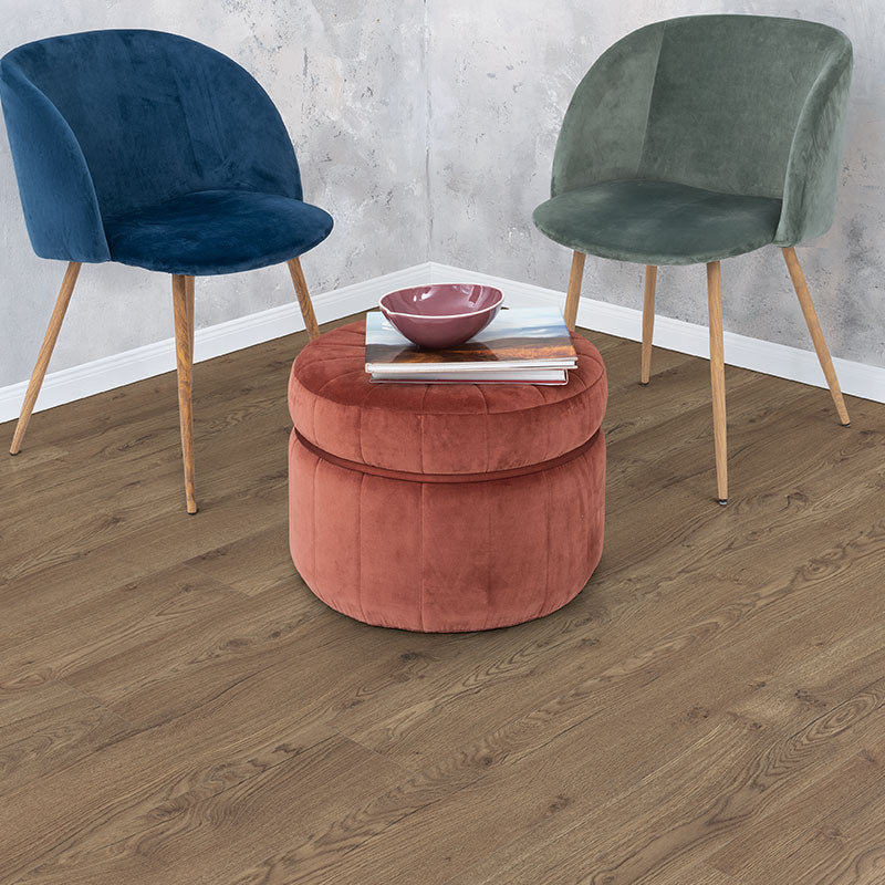 Two upholstered chairs with a round pink ottoman on a wooden floor.