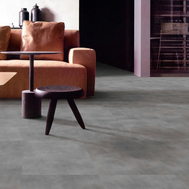 Modern living room with a brown sofa, small round table, and dark gray floor tiles.