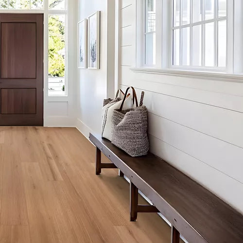Light brown hardwood flooring in a bright, modern entryway with white shiplap walls, a dark wood bench, and a woven basket bag.