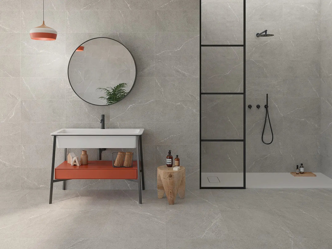 Modern bathroom with gray tiles, a round mirror, and a sink with an orange shelf.