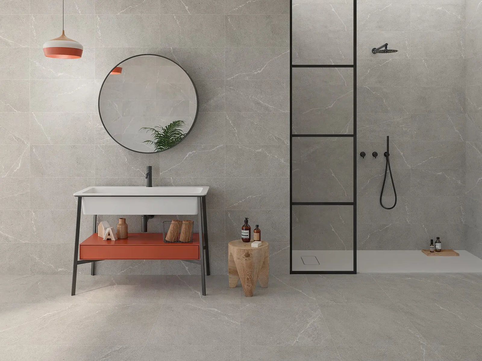 Modern bathroom with gray tiles, a round mirror, and a sink with an orange shelf.