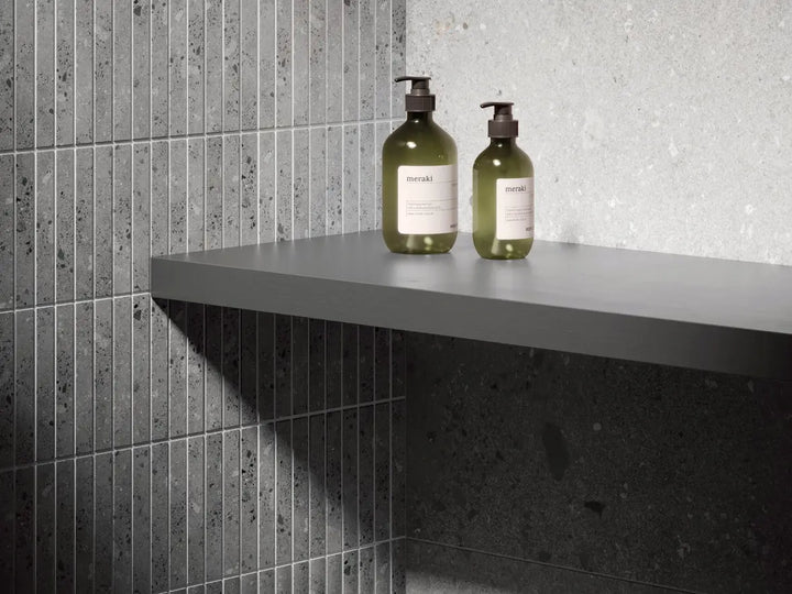 Two bottles on a gray shelf against tiled walls