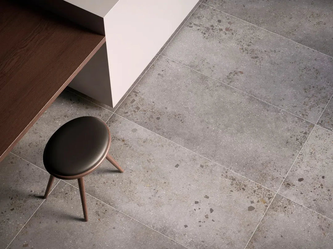 Gray tiled floor with a small brown stool in a minimalistic setting