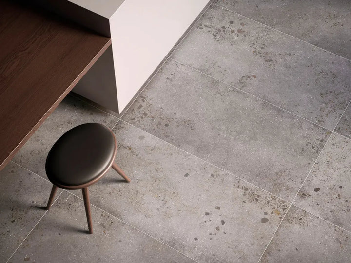 Gray tiled floor with a small brown stool in a minimalistic setting
