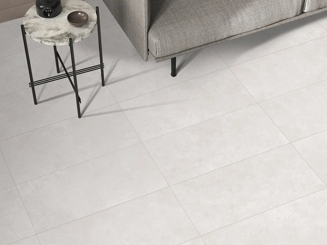 White tiles in a room with a gray sofa and small round table.
