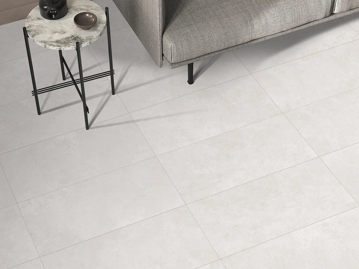 White tiles in a room with a gray sofa and small round table.