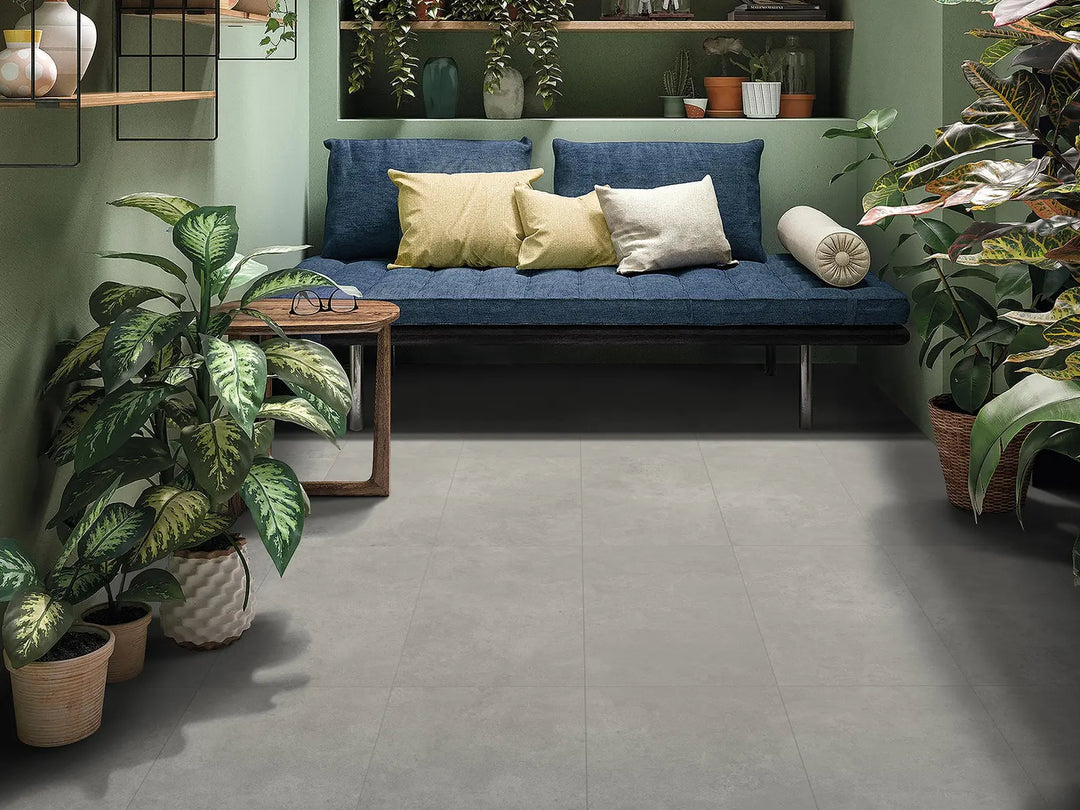 Living room with a blue sofa, cushions, and potted plants on a gray tiled floor.