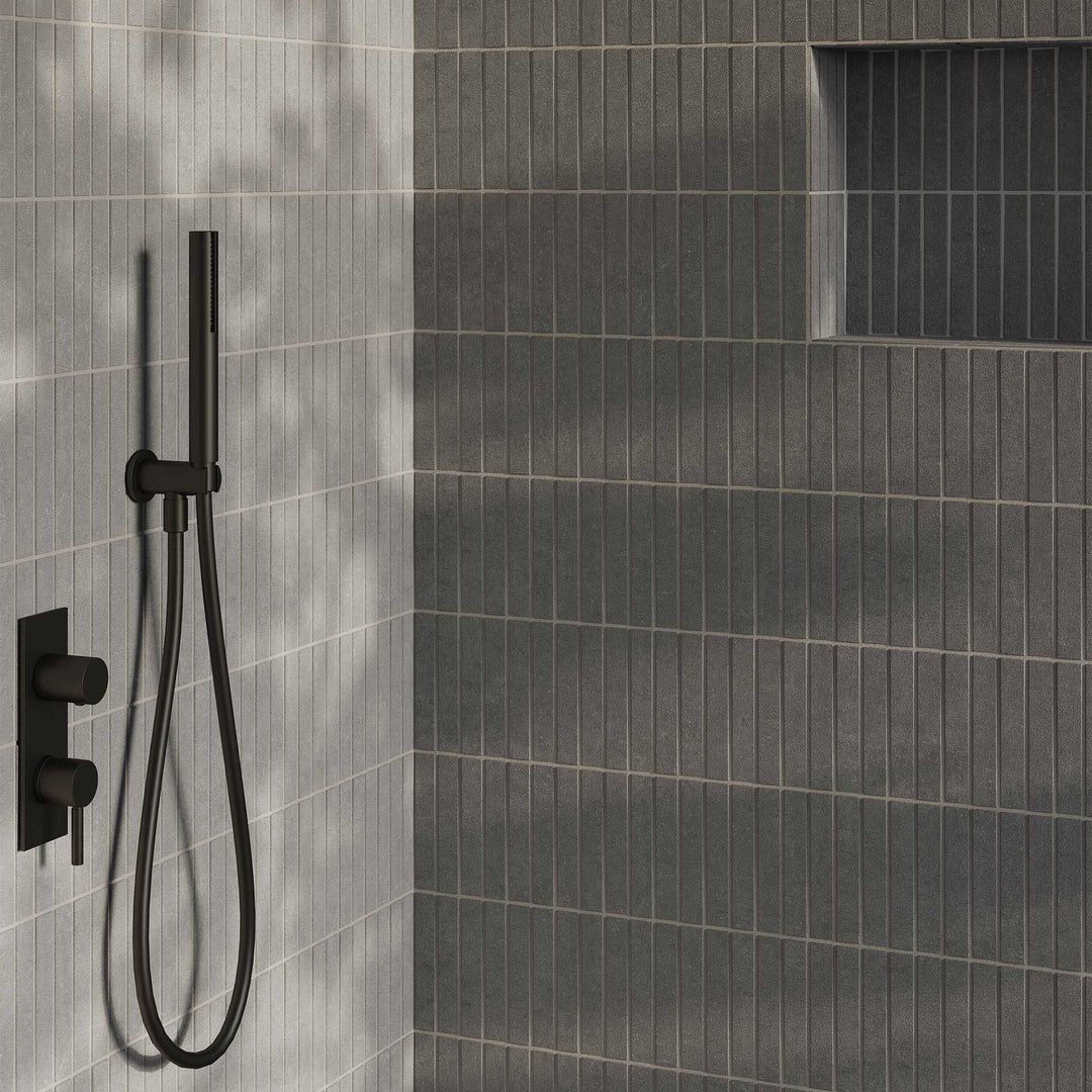 Black shower head and control valve mounted on a gray tiled wall.