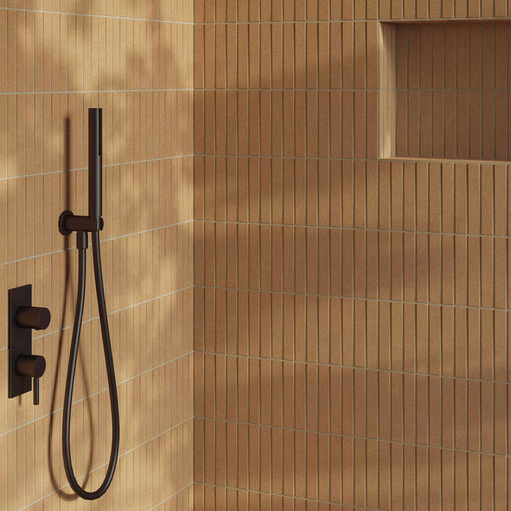 Brown tiled shower with a handheld shower head and control valve.