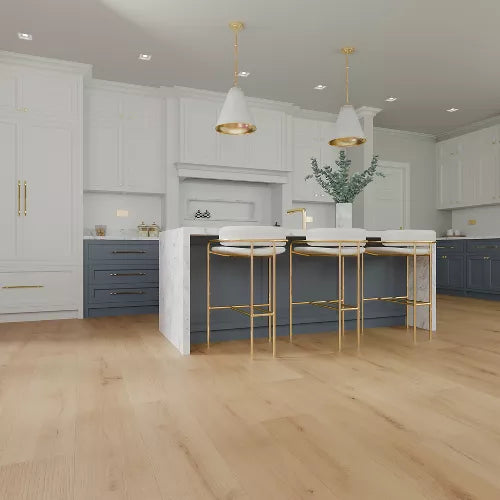 A modern kitchen interior with white upper cabinets, blue-gray lower cabinets, a white island, three white bar stools with gold legs, pendant lights, and light wood flooring.