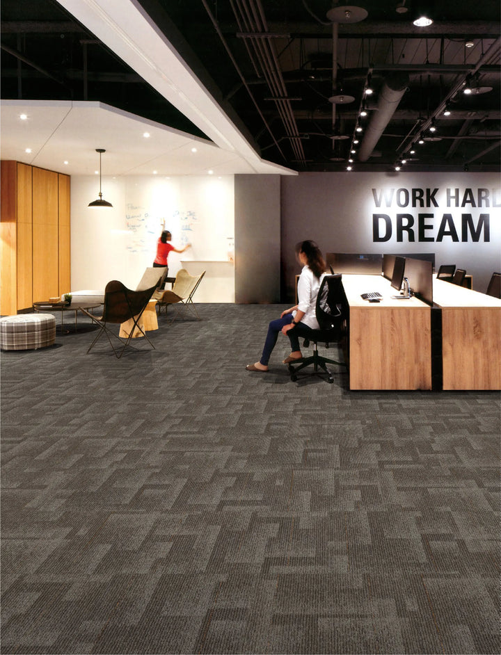 Modern office interior with employees working, motivational quote on wall, and textured gray carpet.