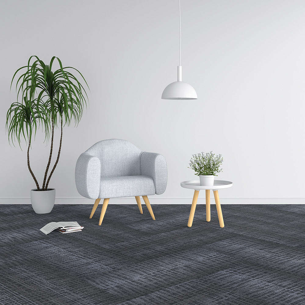 Modern living room with a gray armchair, small table, and plants on a gray carpet.