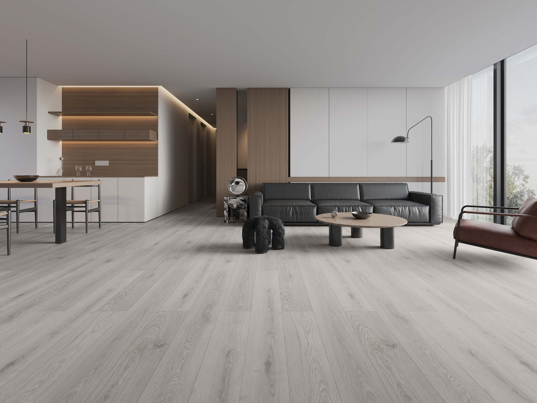 Light gray wood-look laminate flooring shown in a modern, minimalist living room with a black leather sofa. Available at Advanced Flooring Waterloo.