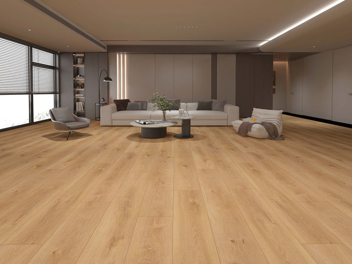 Light oak laminate plank flooring shown in a modern, minimalist living room with a white sofa, gray armchair, and neutral-toned walls. Available at Advanced Flooring.