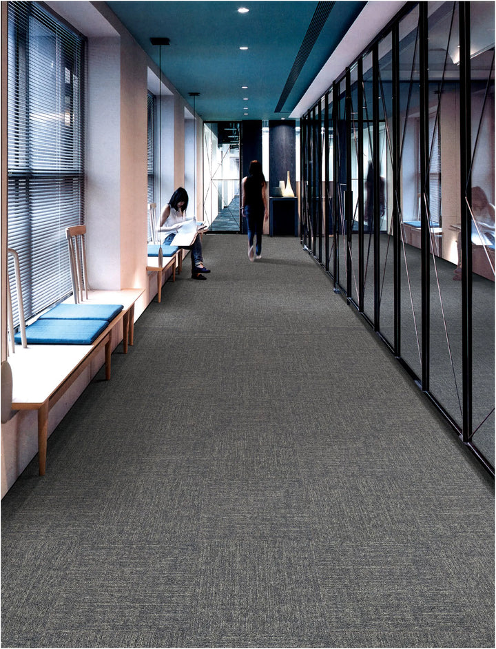 Long hallway with gray carpet, glass walls, and people sitting on benches.