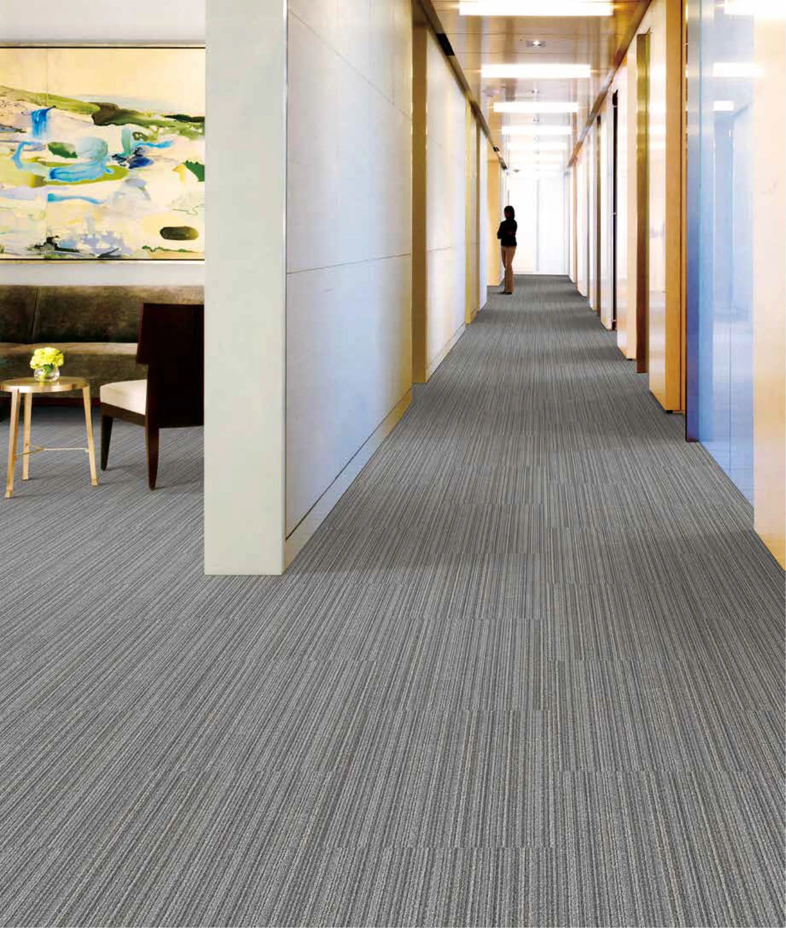 Long hallway with gray carpet and a person walking towards the light