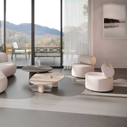 Modern living room with round beige chairs and tables, large windows with a view of mountains.