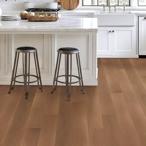 Light brown hardwood flooring in a bright, modern kitchen with white cabinets, a marble island, and two metal bar stools.