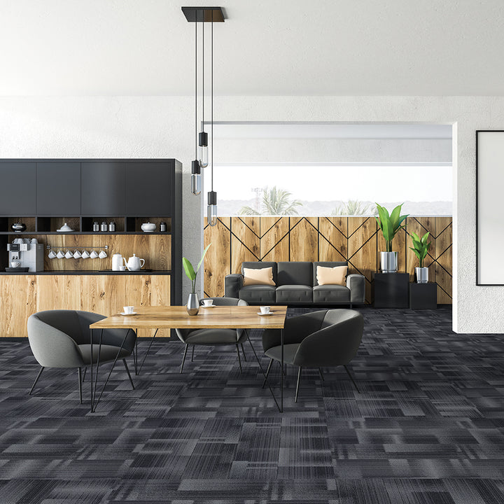 Modern living room with gray sofa, wooden dining table, and geometric patterned carpet.