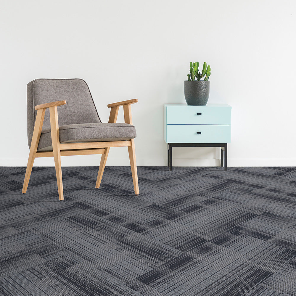 Gray patterned carpet tiles with a chair and side table in a room setting.