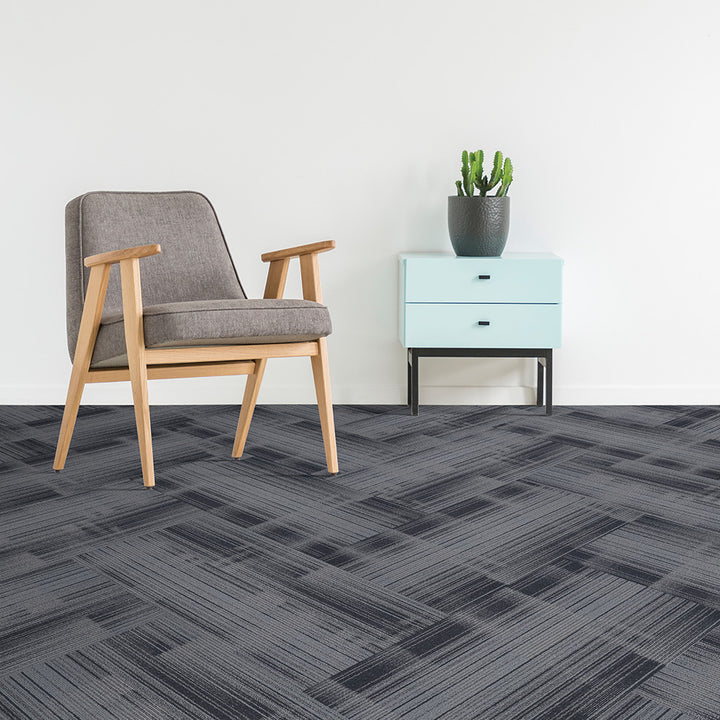 Gray patterned carpet tiles with a chair and side table in a room setting.
