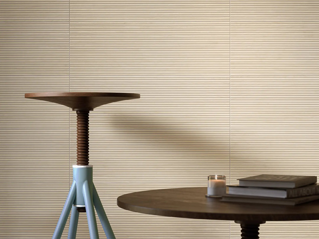 Round wooden table with a candle and books against a beige wall with horizontal blinds.