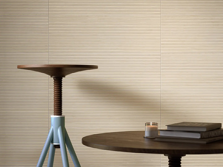 Round wooden table with a candle and books against a beige wall with horizontal blinds.