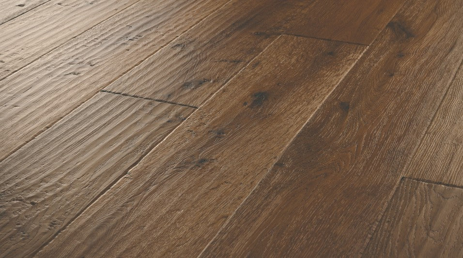Close-up of Bronze Dust engineered hardwood flooring from the Atelier Collection featuring hand-scraped white oak with dark brown tones and 3 mm veneer.