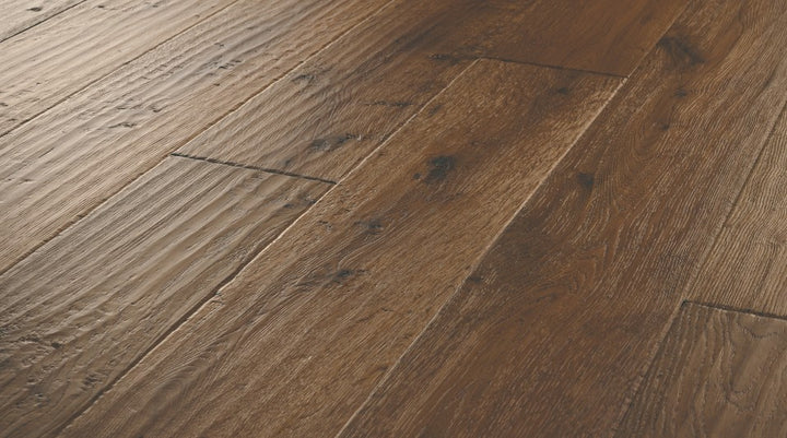 Close-up of Bronze Dust engineered hardwood flooring from the Atelier Collection featuring hand-scraped white oak with dark brown tones and 3 mm veneer.
