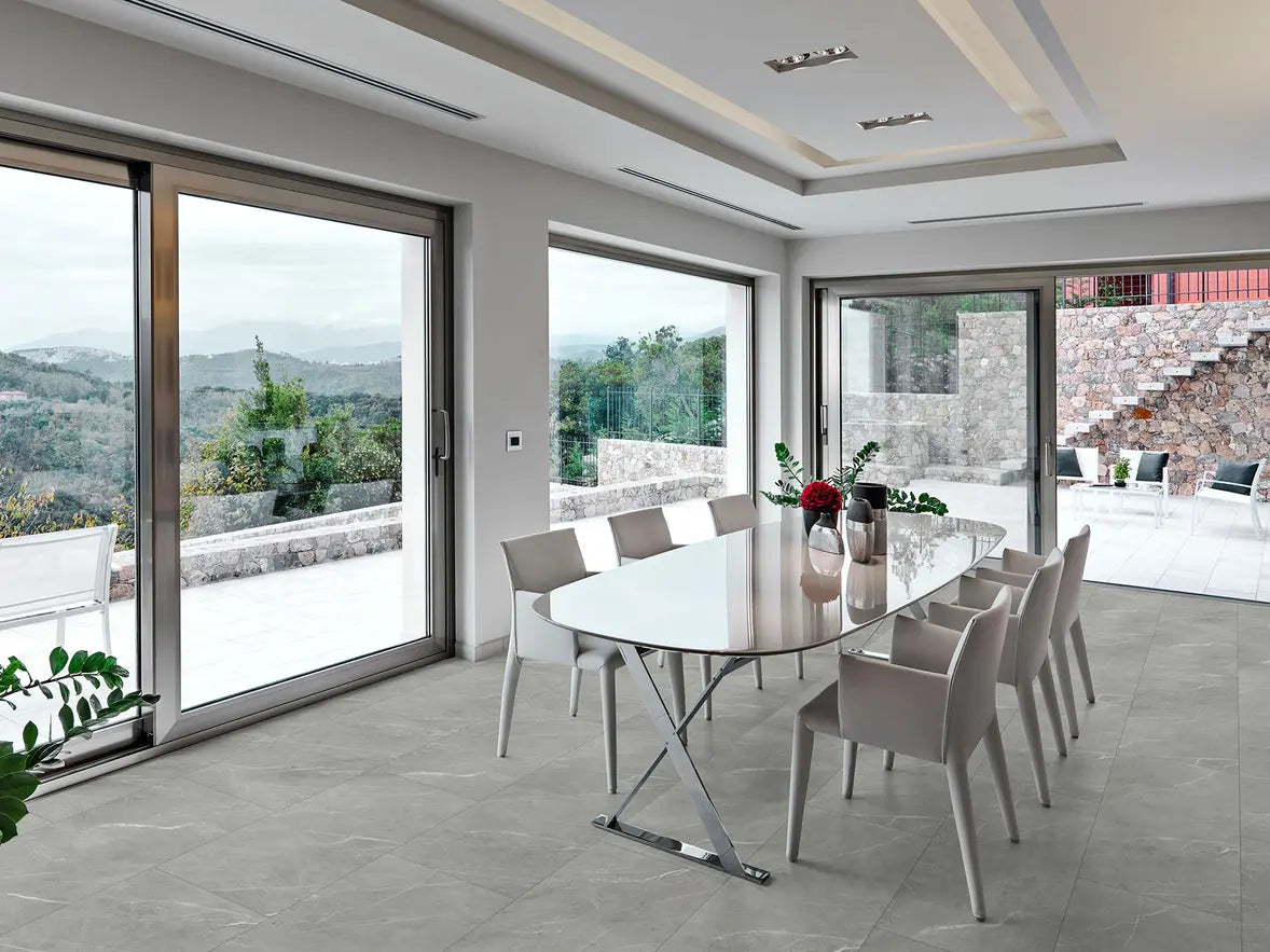 Modern dining area with a glass table and chairs near large windows with a view of a scenic landscape.