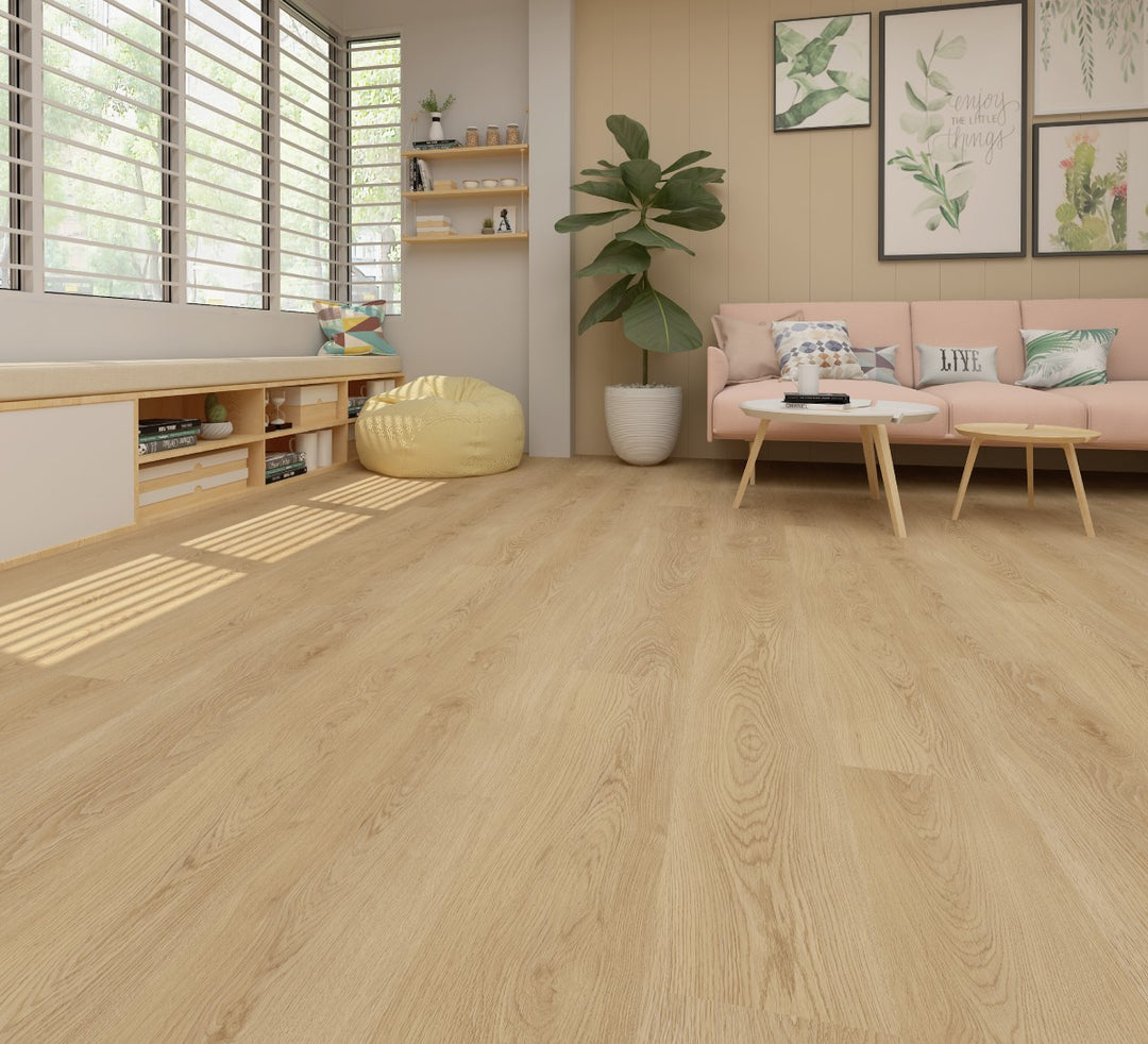 Light oak wood flooring shown in a modern, sunlit living room with a pink sofa, green plant, and wooden shelves.